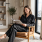 A woman sits in a wooden armchair by a window, reading a book while wearing a black pajama set. The image includes the text 'Black' in the upper left corner, indicating the color option.