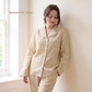 Woman wearing beige pajamas leaning against a wall with 'Buttermilk Glow' text.
