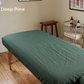 A dark green massage table cover or sheet spread across a treatment table in a spa-like room with a wooden stool, metal cart, and wood floor. The text 'Deep Pine' appears in the upper left corner.