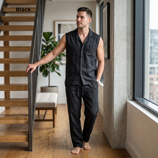 A man wearing a black sleeveless button-front shirt and matching black pants stands barefoot in a modern indoor hallway with wood floors, a staircase, and a large window. The word 'Black' appears in the top-left corner.
