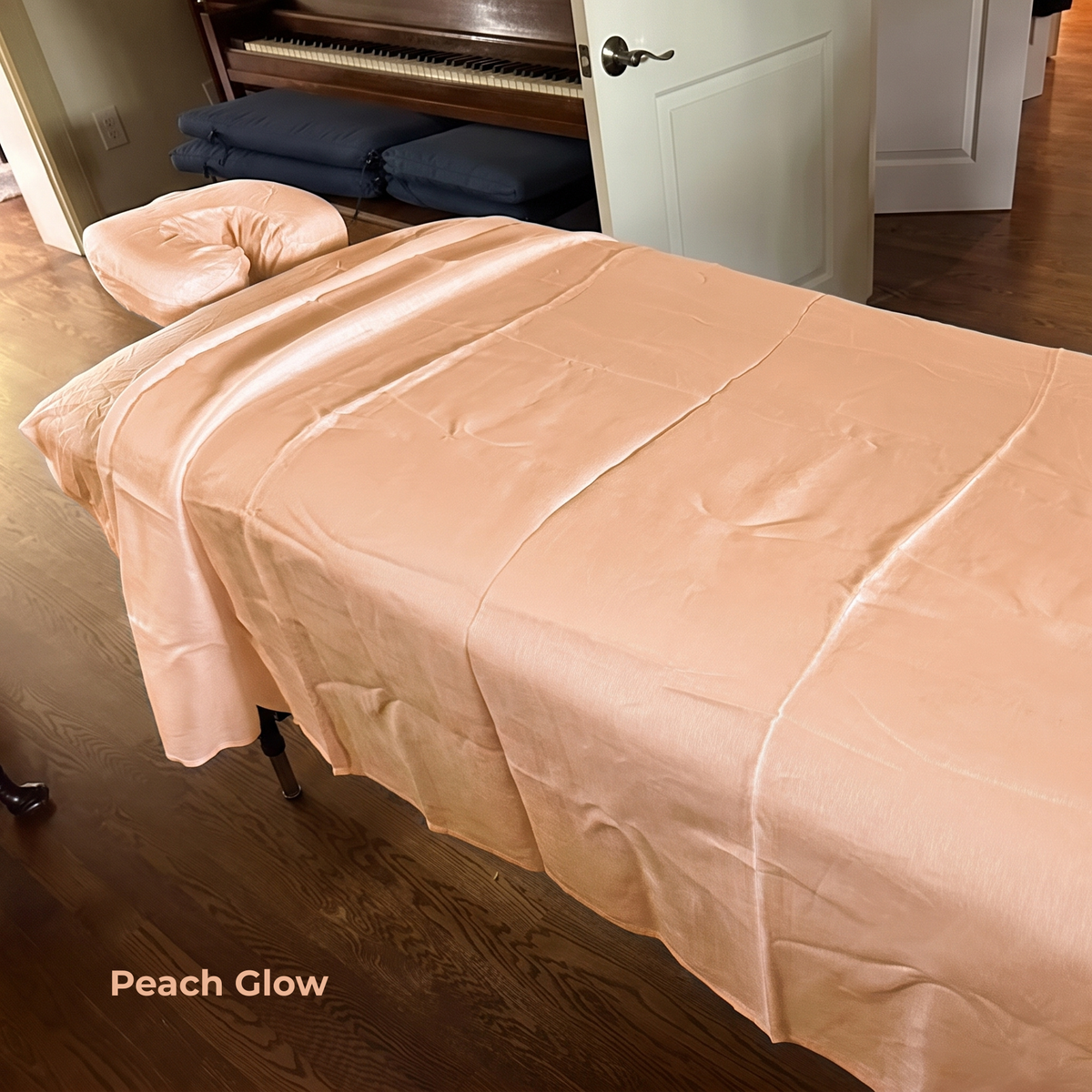 A peach satin sheet draped over a massage table in a room with hardwood floors and a piano in the background. The text 'Peach Glow' is visible in the bottom-left corner.
