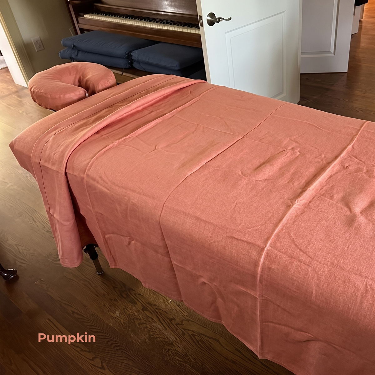 A peach-pink massage table cover draped over a treatment table in a home office setting, with a matching headrest pillow. The text 'Pumpkin' is visible in the bottom left corner.