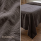A dark brown linen sheet or bedspread shown draped over a bed in a bedroom setting, with a close-up fabric texture panel on the left. Text on the left reads 'Smoked Obsidian'.