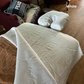 A white U-shaped neck pillow and matching white pillowcase are displayed on a bed with a white sheet, alongside a brown blanket and a red armchair in a home setting. The word 'White' is written in the top right corner.
