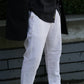 A person wearing white trousers and a black jacket, photographed outdoors on a paved walkway with greenery visible.